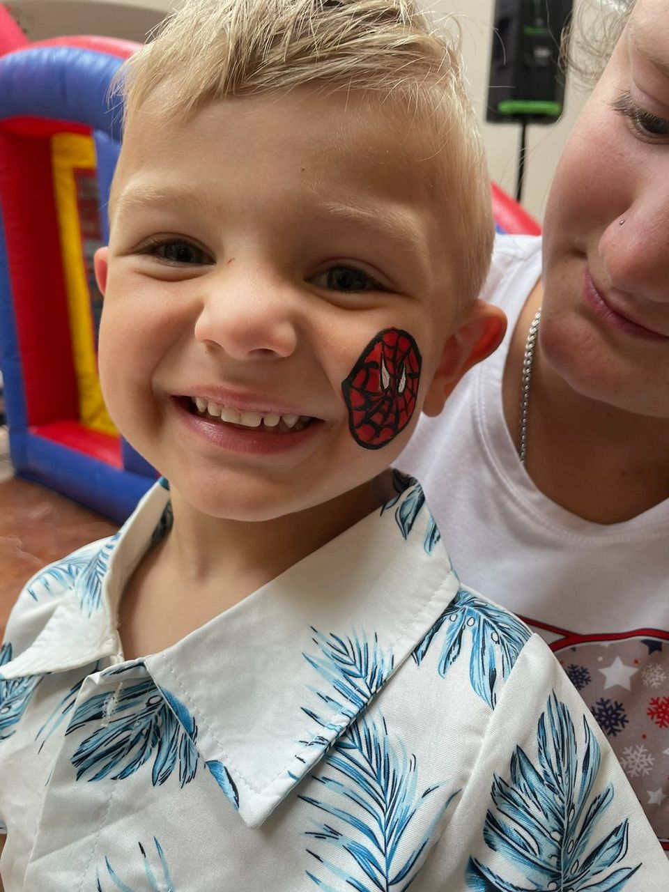 Smiling child with face paint at an indoor play area, wearing a white patterned shirt