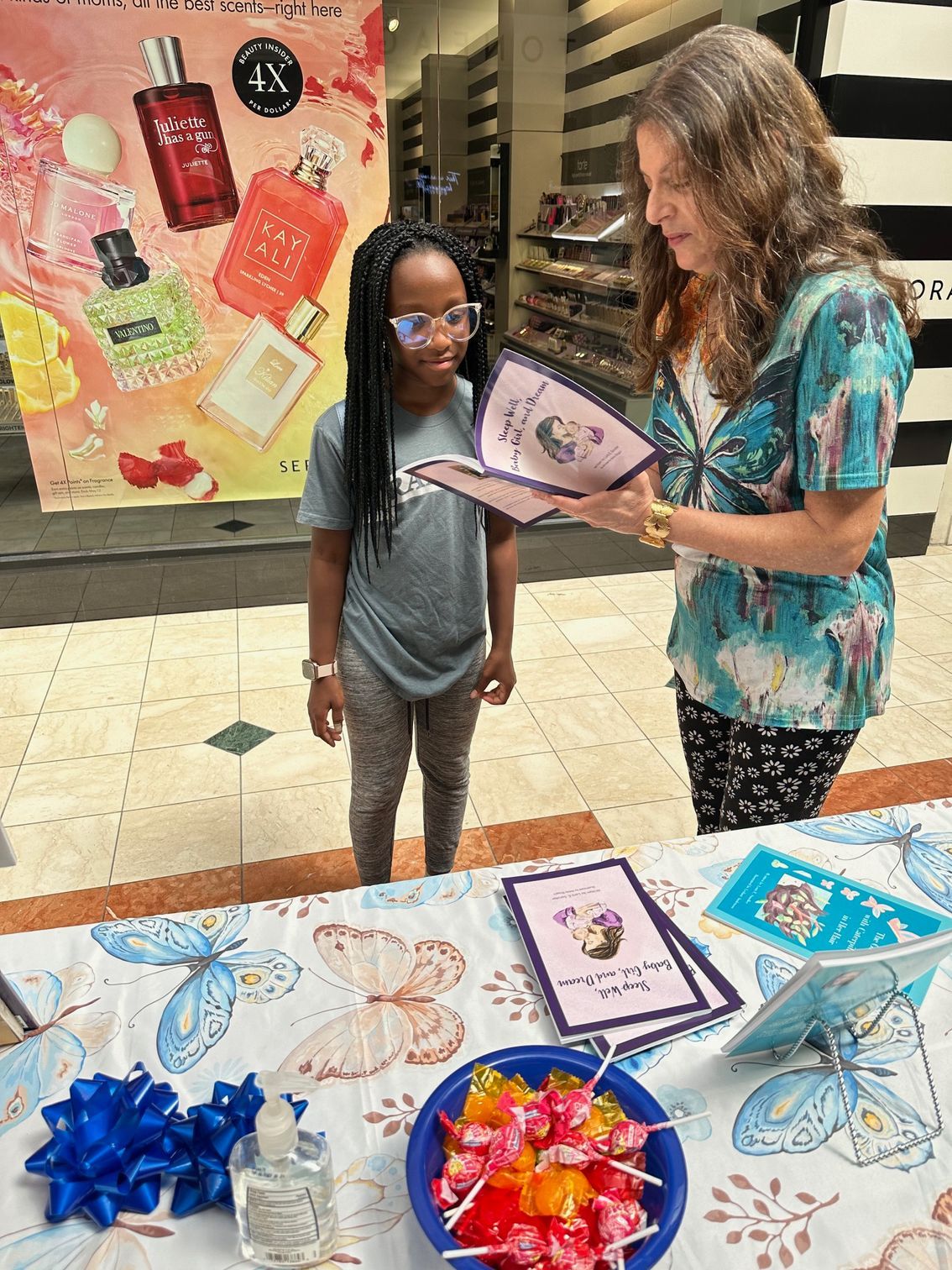 Teacher showing a child a book at a decorated table with bows and butterfly crafts in a school hallway