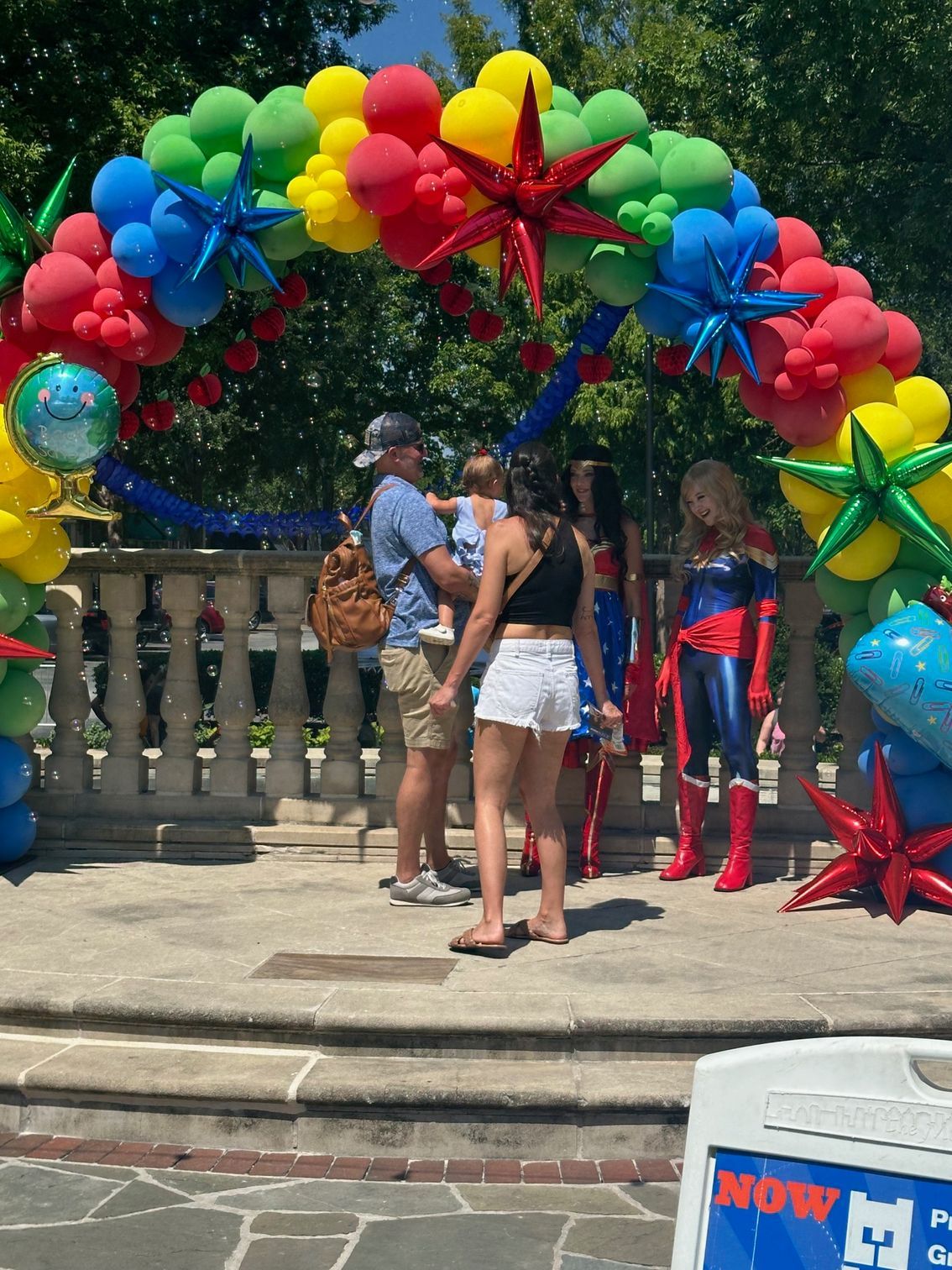 People standing under a colorful balloon arch at an outdoor celebration