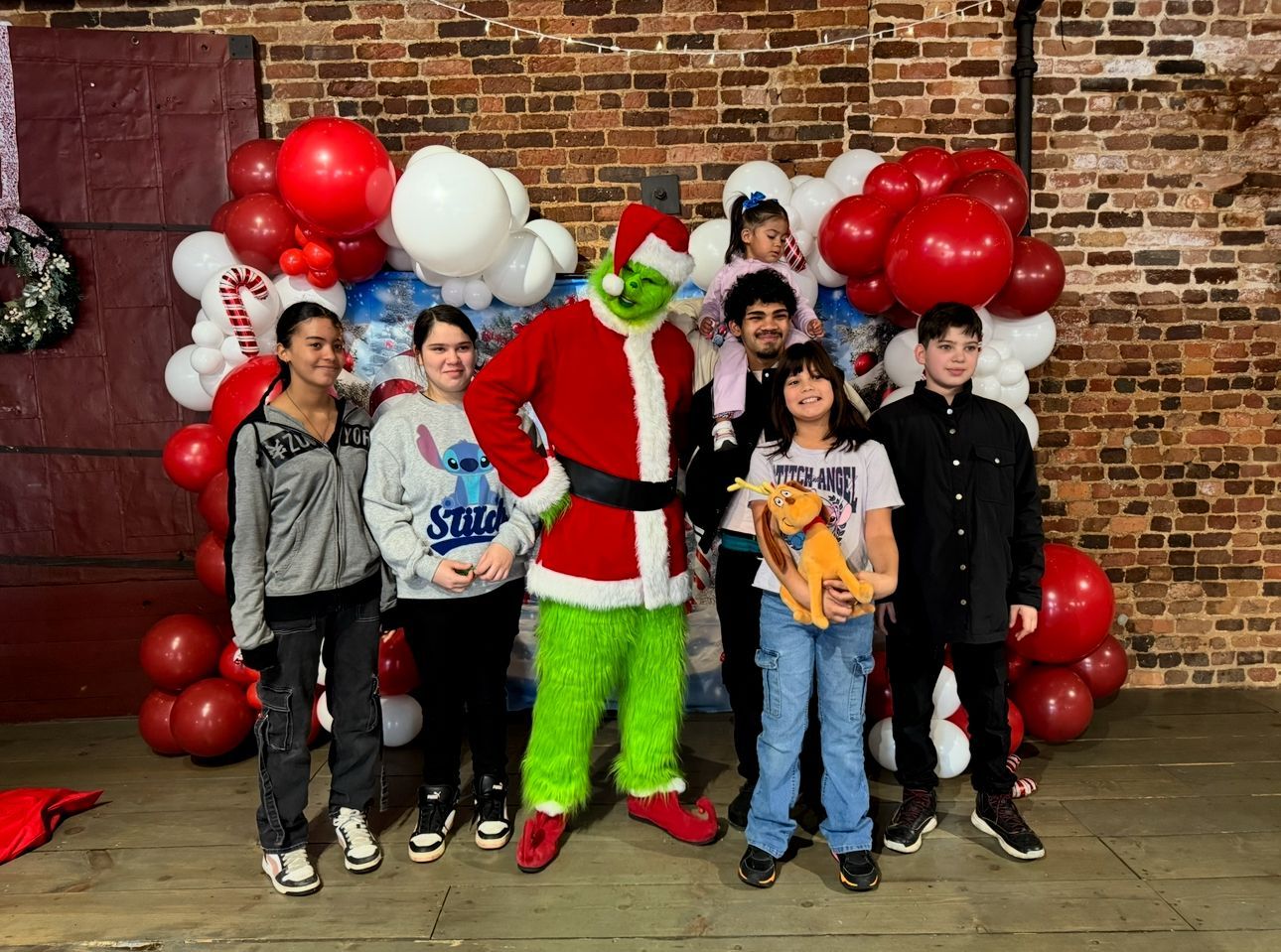 Group posing with Santa in front of a brick wall and red-and-white balloon arch