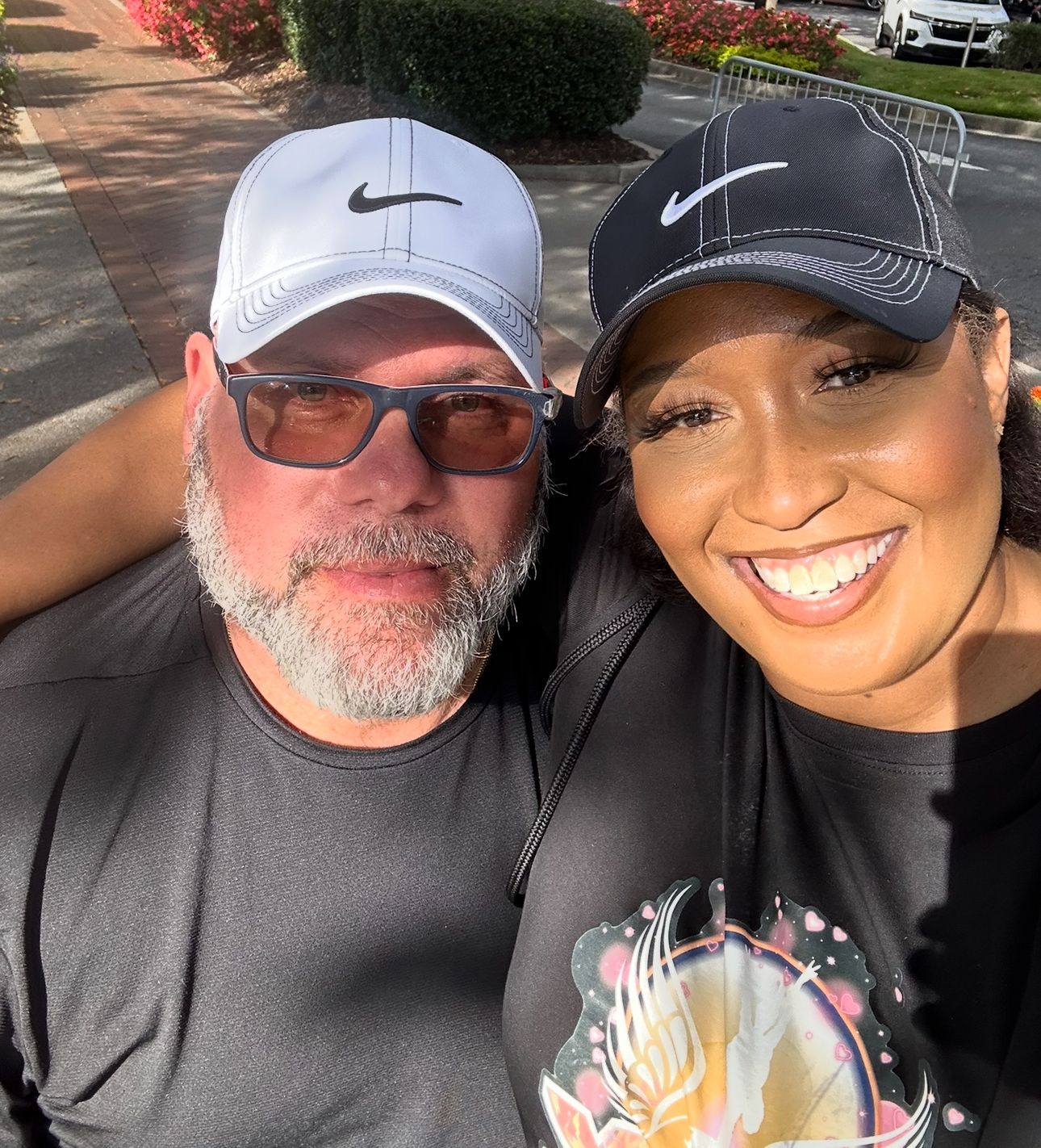 Two smiling people in Nike caps taking a selfie outdoors in sunlight.