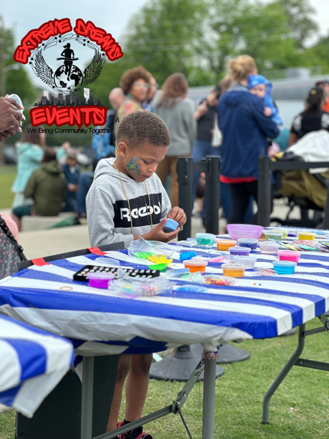 Child painting at a striped outdoor table during a community event