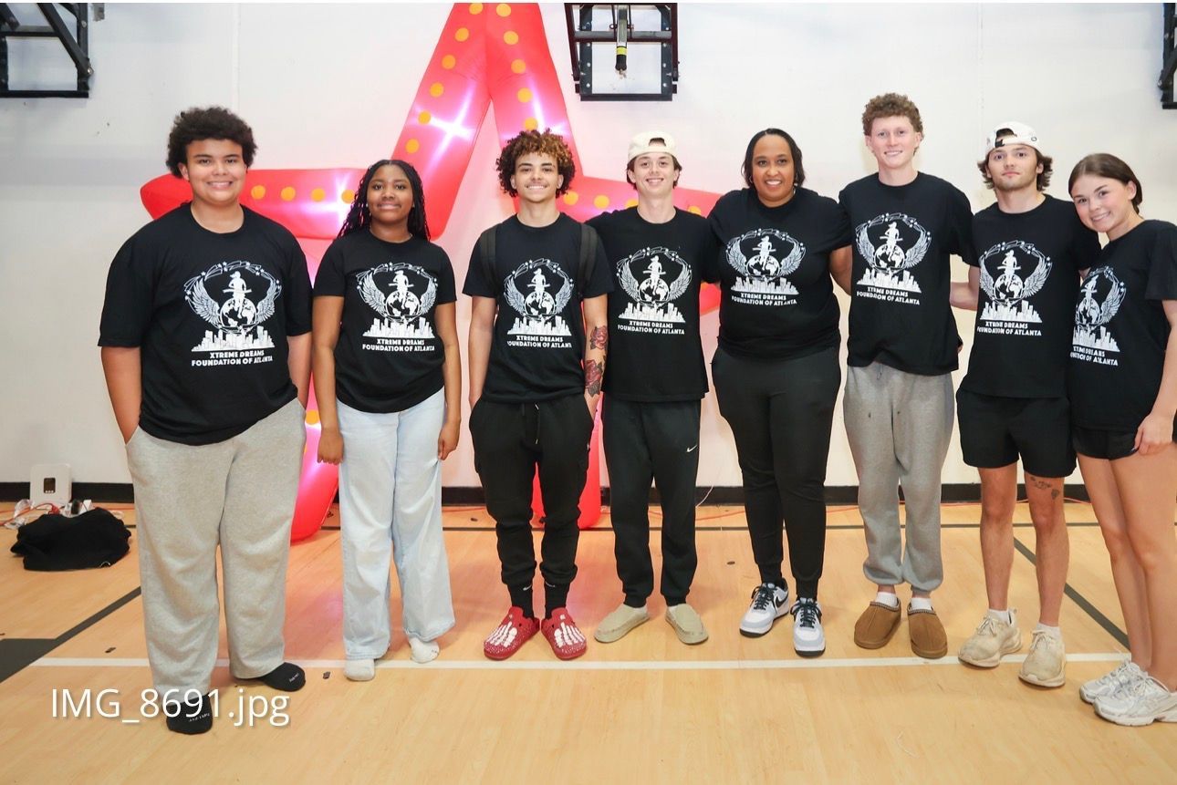 Seven people in matching black T-shirts posing indoors in front of a red-lit triangular backdrop