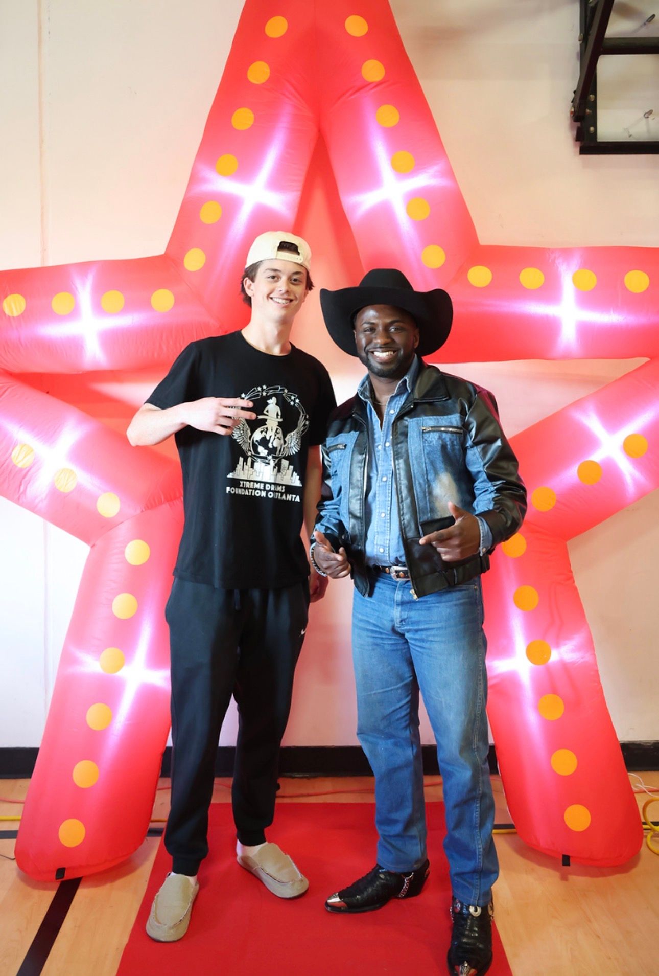 Two people posing in front of a large pink star with lights indoors