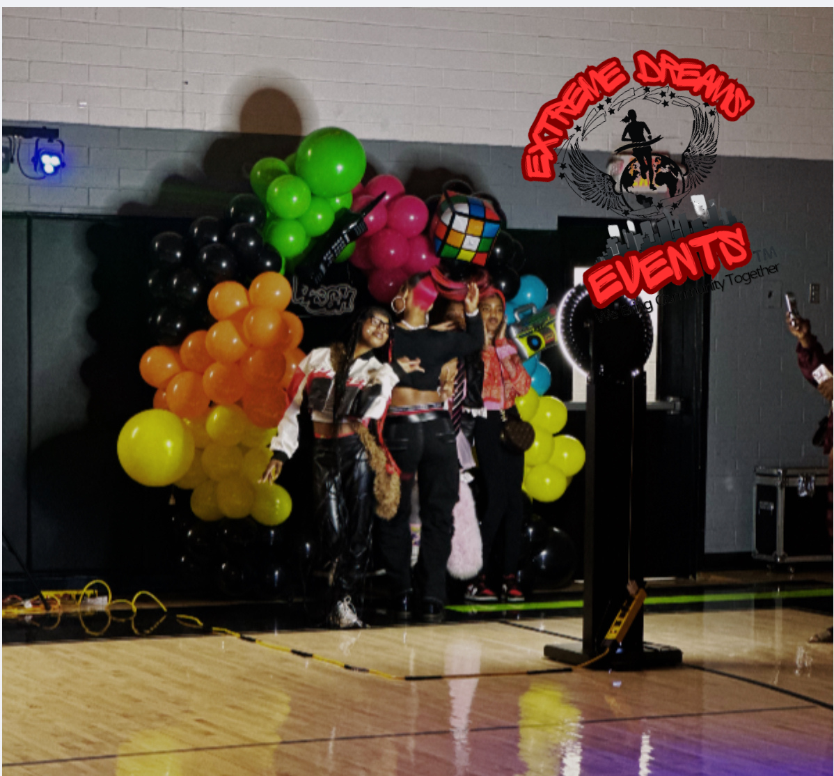 Children emerging with colorful balloons at an indoor event stage, with a black backdrop and “Events” sign