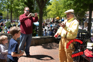 Street performer in yellow hat playing a small instrument for a crowd in a park