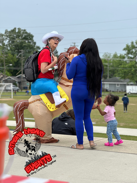Clown on a yellow hobby horse greets a woman and child outdoors at a community event