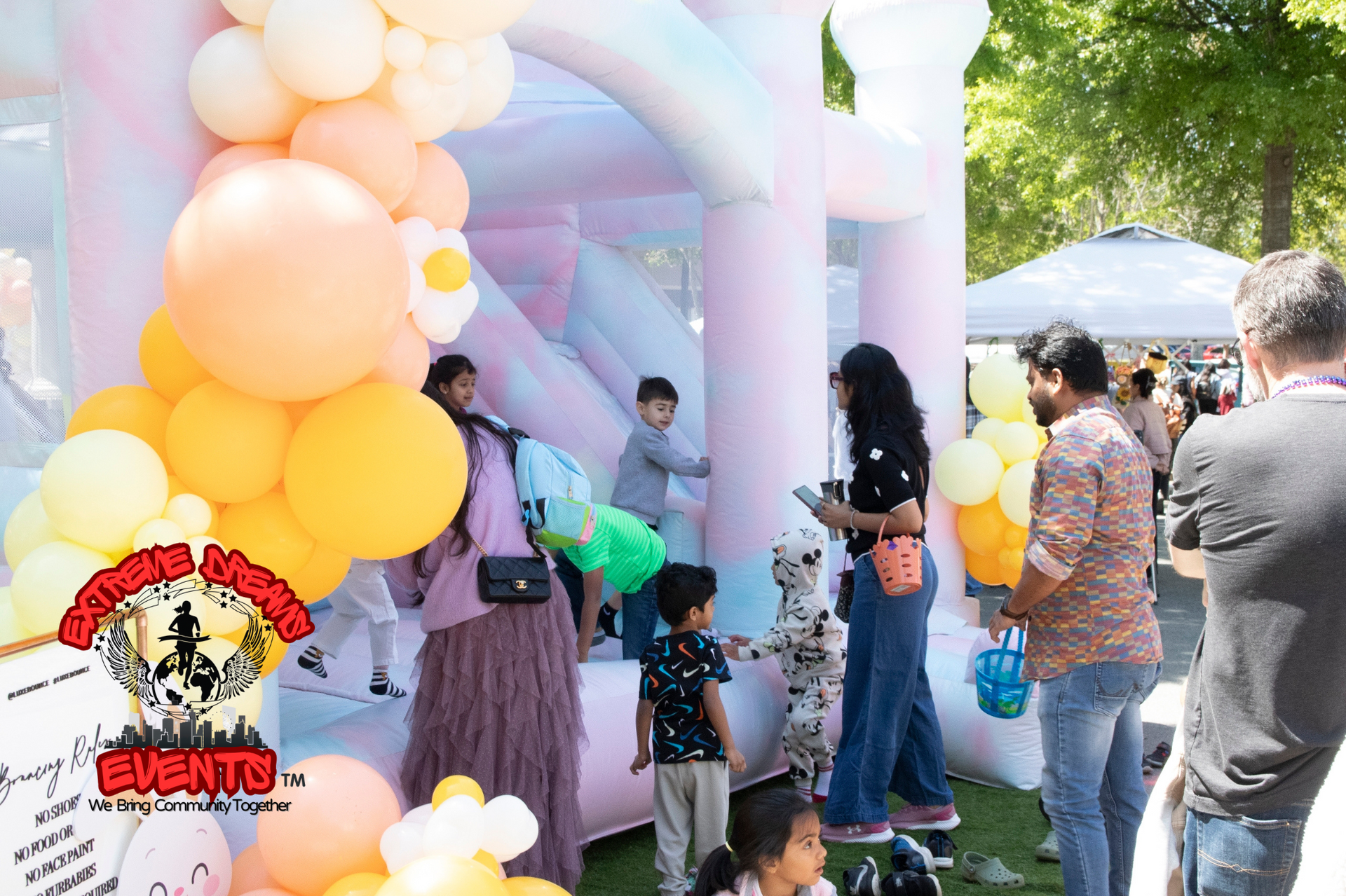 People waiting at a pastel balloon arch entrance at an outdoor event, with a pink backdrop and balloons.