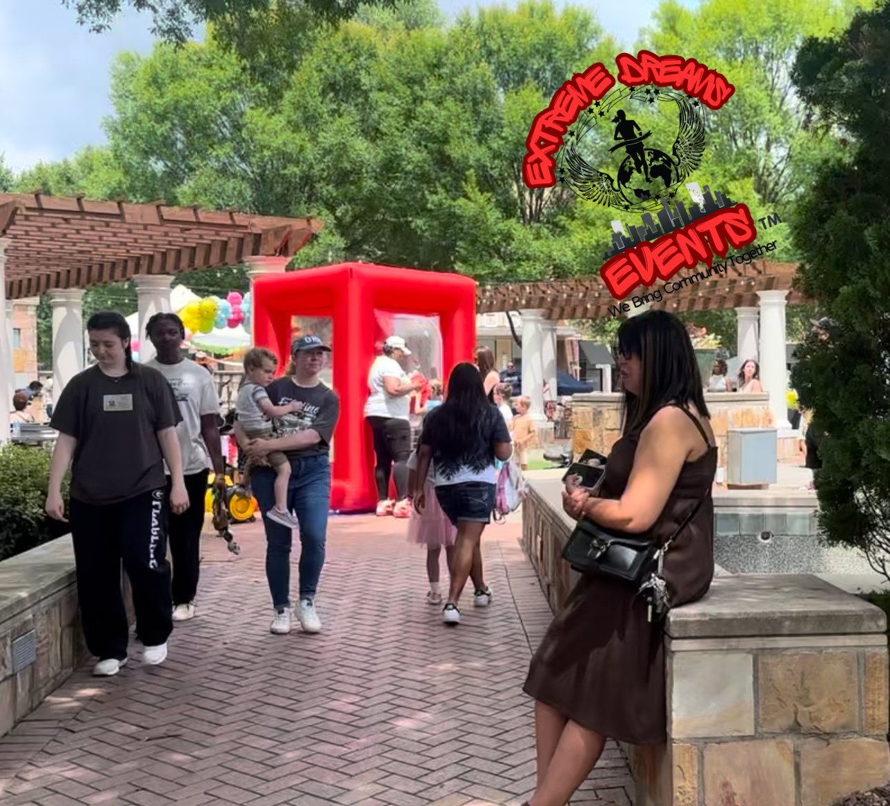 Outdoor event entrance with a red inflatable arch and people walking on a brick path.