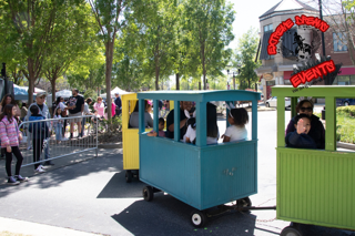 Small amusement park train with children riding on blue and green cars along a tree-lined path