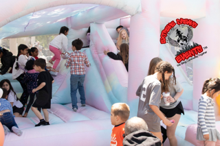 Children playing on a pink and white inflatable bounce house at an outdoor event