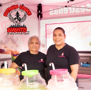 Two people behind a booth with clear jars and colorful lids at an event stand