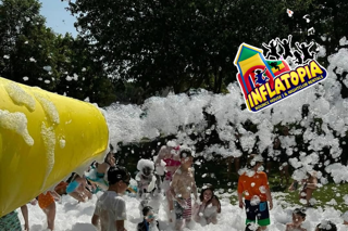 Kids play in a foam-filled inflatable park with a yellow slide and colorful Inflatopia sign.
