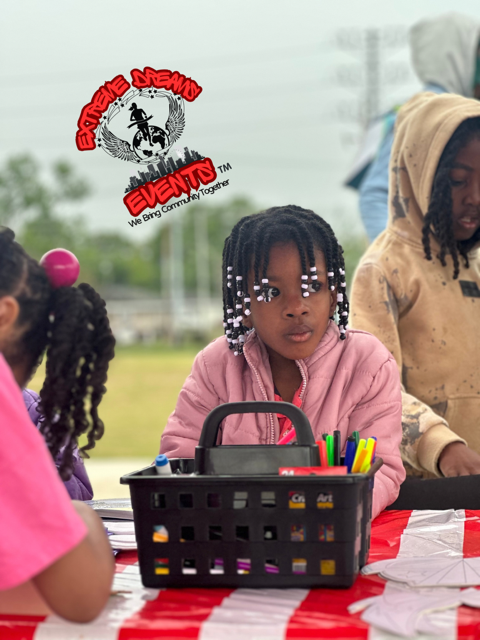 Children seated at a table with a pencil holder at an outdoor event.