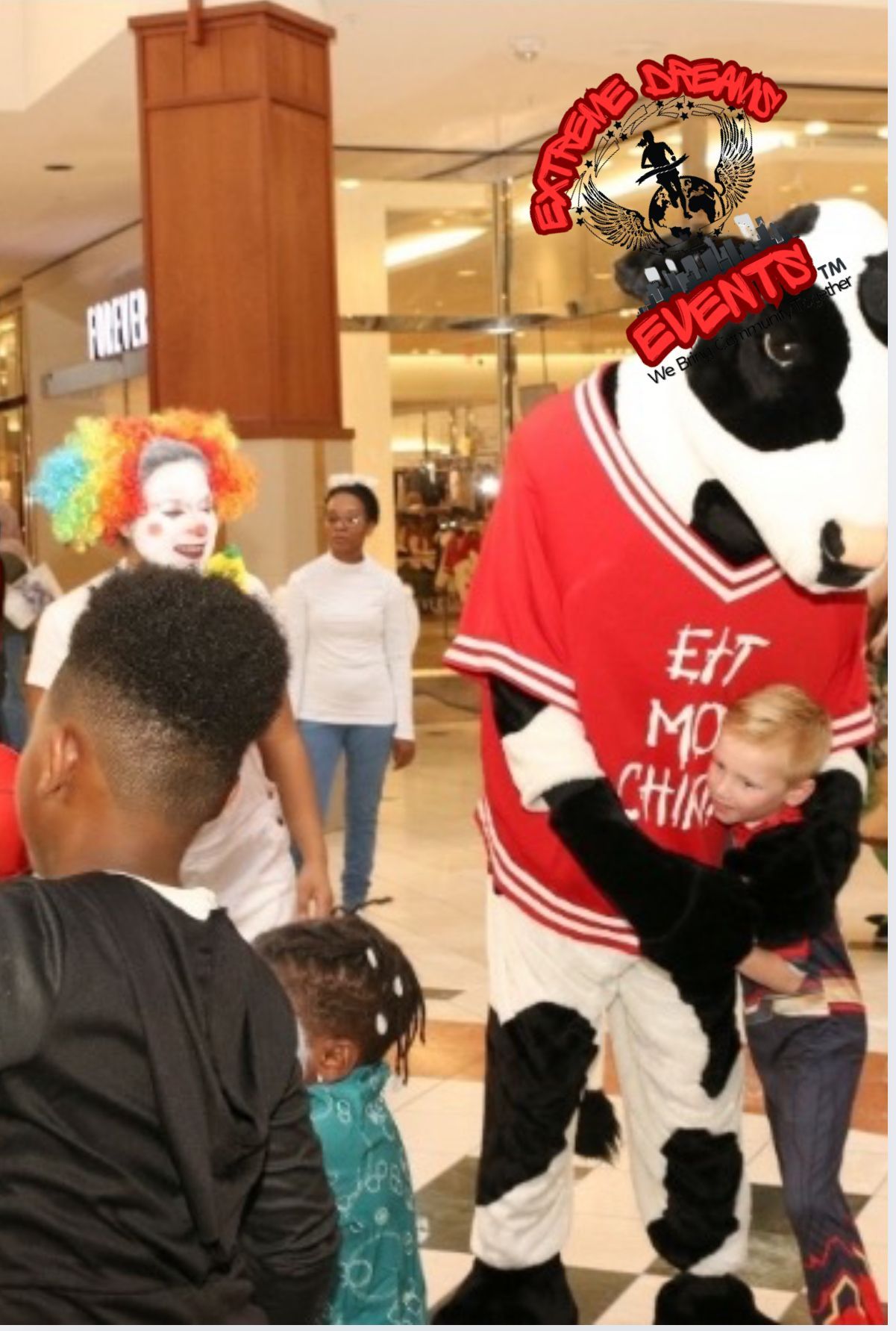 Costumed cow mascot in red shirt greeting children at an indoor holiday event
