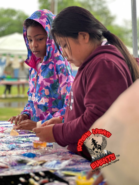Two people sort items on a table at an outdoor event, one in a colorful hoodie and one in a maroon sweater.