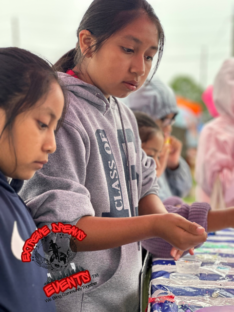 Children in hoodies looking down at an outdoor activity table with colorful materials