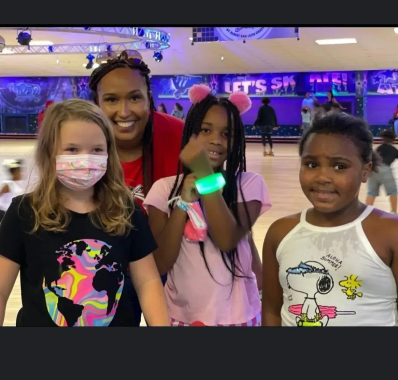 Four people smiling at a roller rink, with neon lights and skate rentals in the background