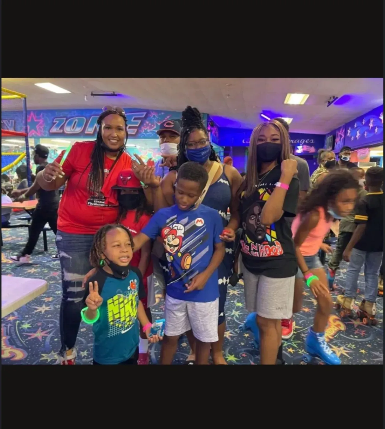 Group posing together at an arcade, smiling and making peace signs amid colorful game lights.