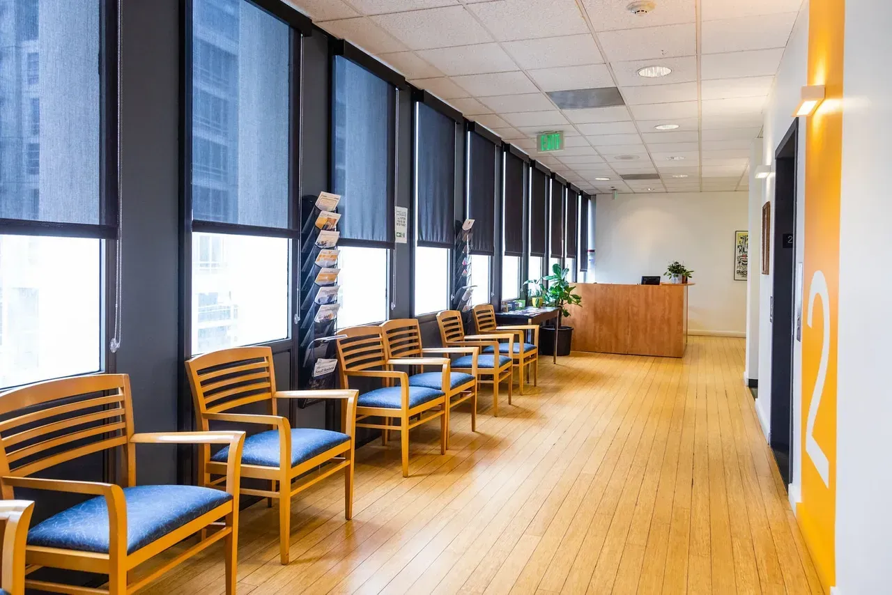 Empty modern office hallway with blue chairs, wood floors, and large windows