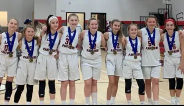 Girls' basketball team in white uniforms standing in a line with medals after a game