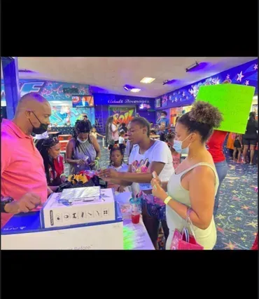People gathered at a colorful arcade counter, interacting with a staff member under bright neon lights.