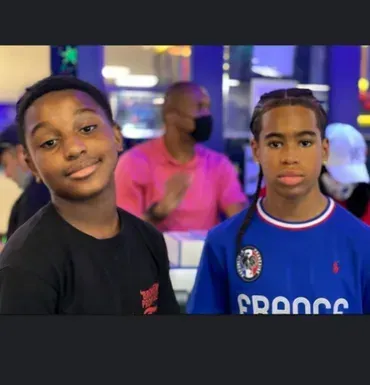 Two children posing indoors, one in a black shirt and one in a blue France jersey, with colorful lights behind them