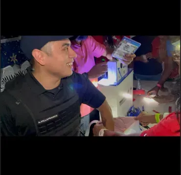 Man smiling at a table while holding cash during a colorful nighttime celebration