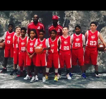 Youth basketball team in red uniforms posing outdoors, with coaches behind them.