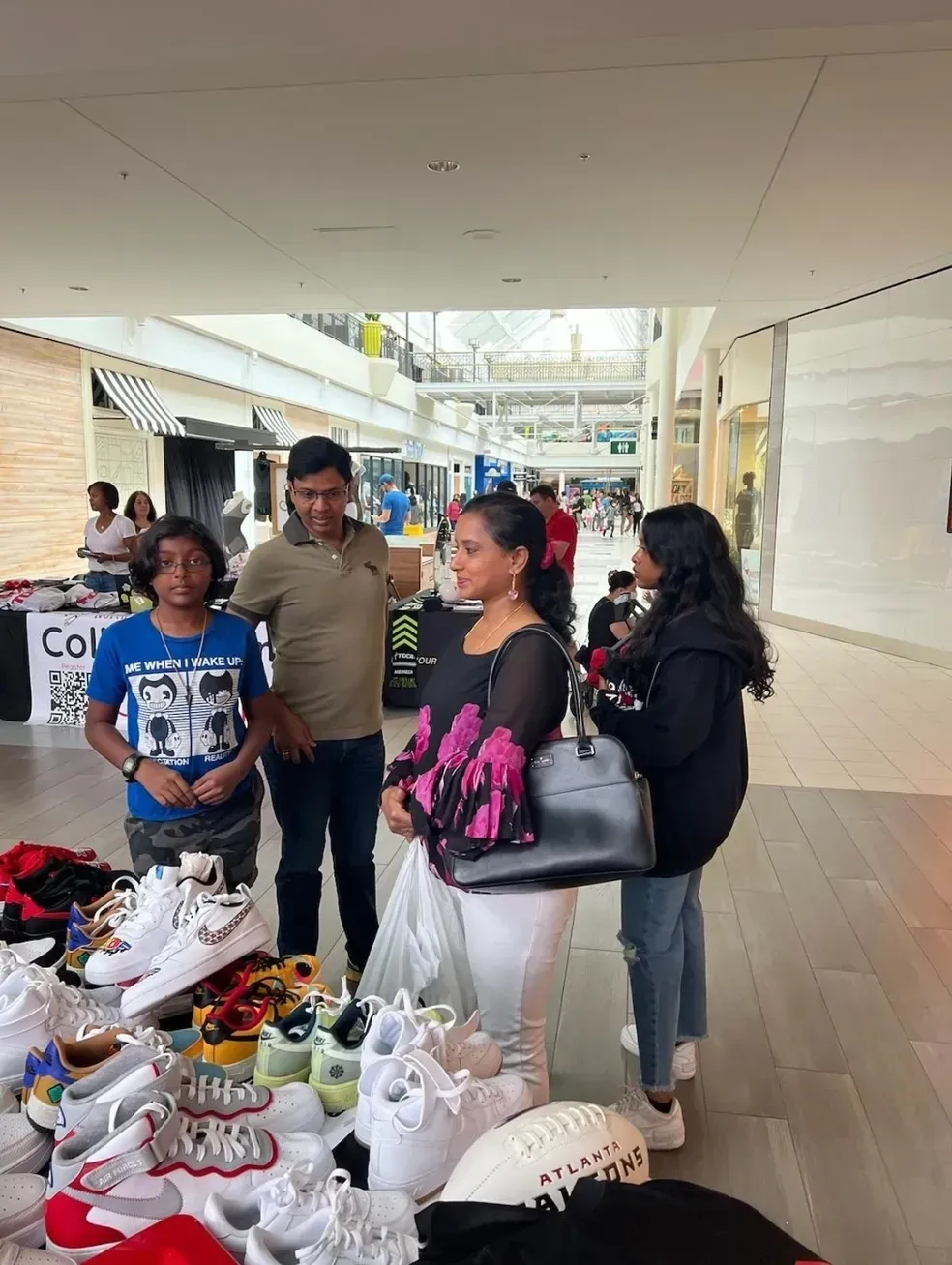 People browsing shoes at a market stall in a covered shopping corridor