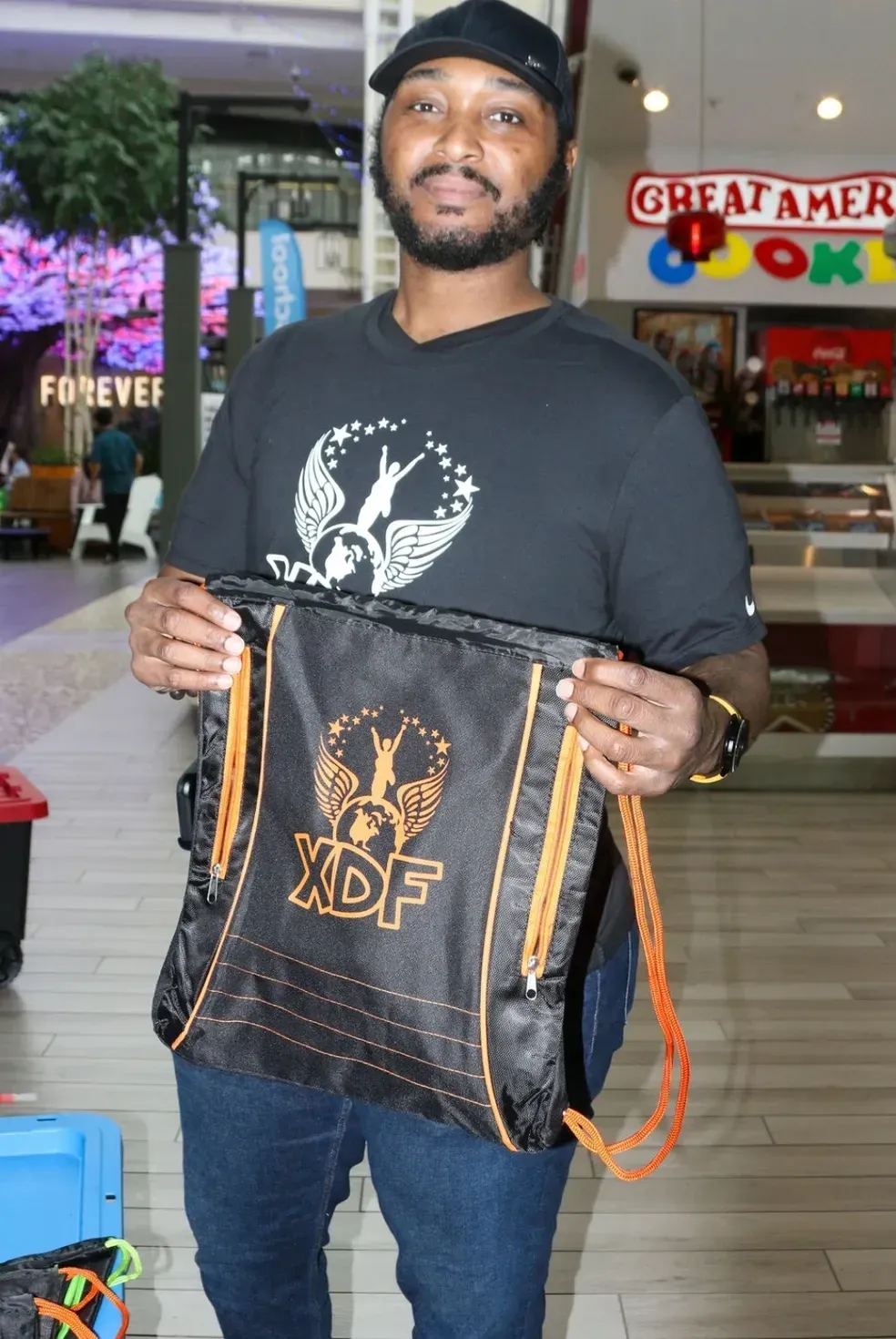 Man holding a black drawstring bag with gold logo inside a mall corridor