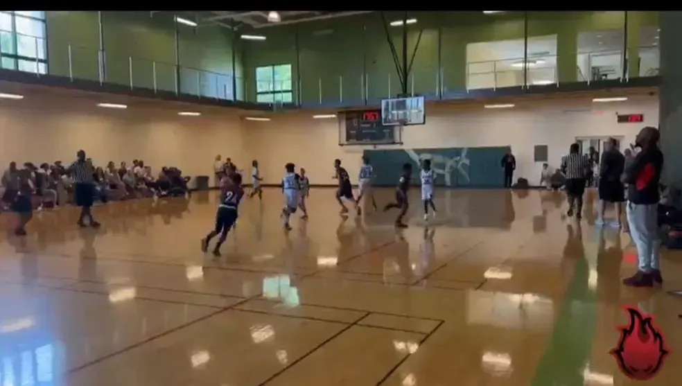Indoor gym basketball game in progress, with players running on a polished court.