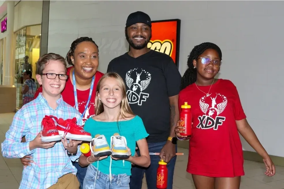Five people smiling indoors, holding candles and small items in a lobby.