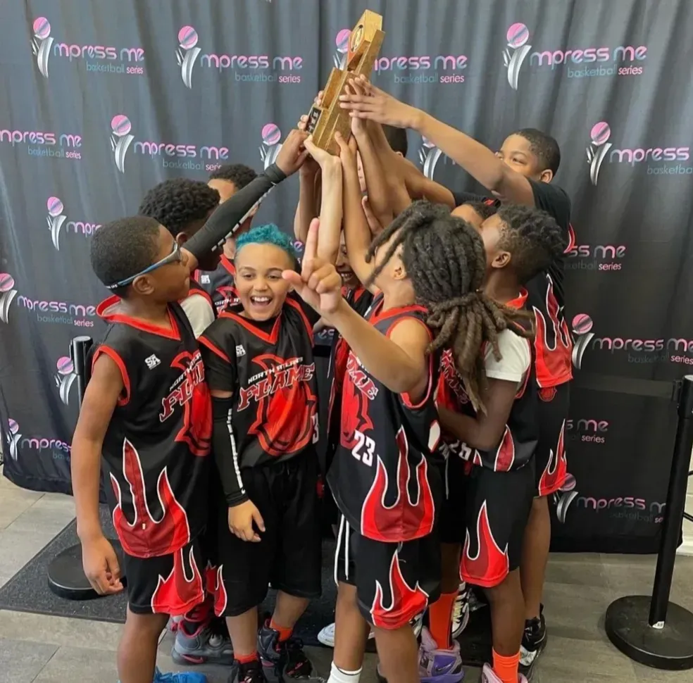 Youth basketball team in black-and-red uniforms raising a trophy in celebration
