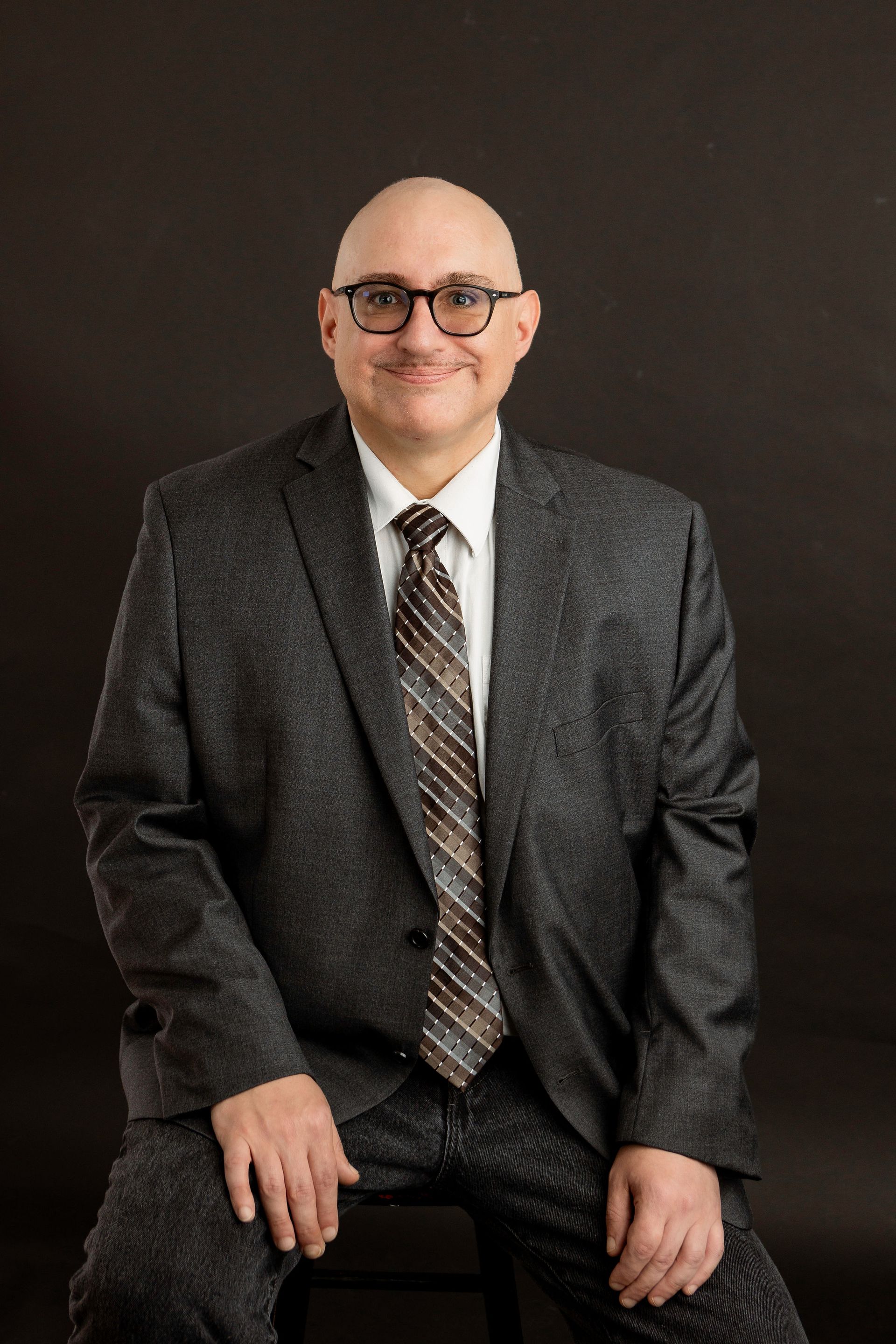 Man wearing glasses, white shirt, and pink tie in an office setting, looking at the camera.