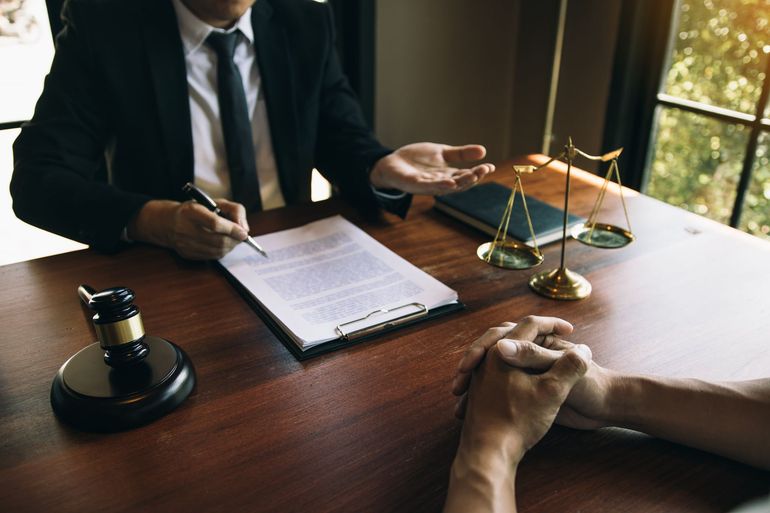 Lawyer meeting at desk with scales of justice, notepad, and gavel, speaking with a seated client