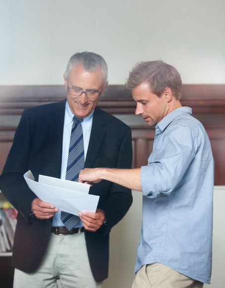 Two people reviewing papers together in an office, one in a suit and one in a blue shirt.