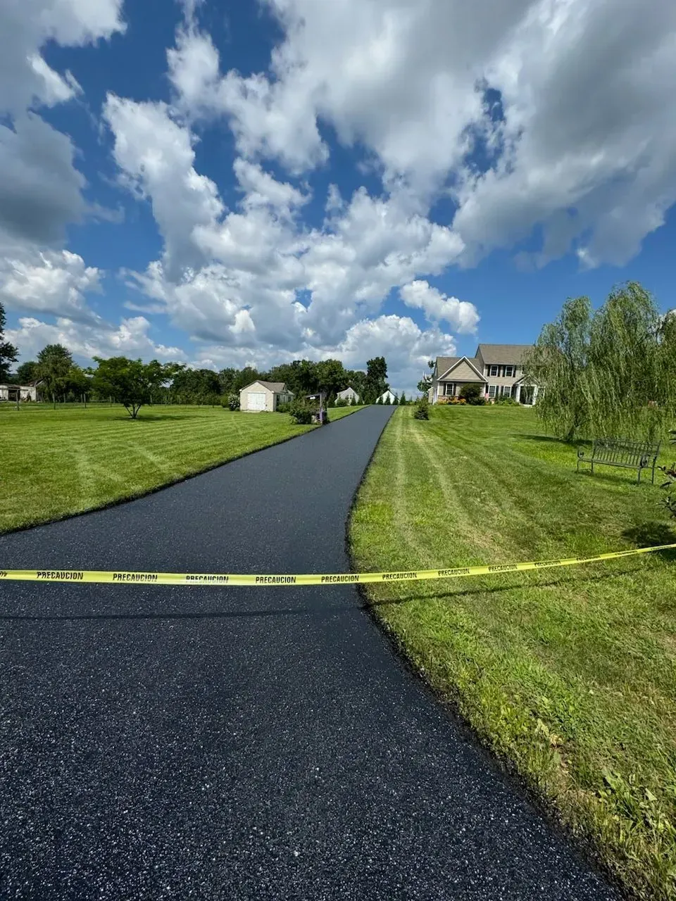 New asphalt driveway blocked by yellow caution tape leading to a house under a cloudy sky