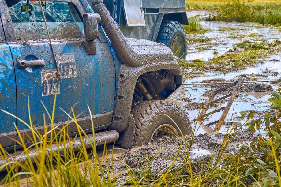 Blue off-road vehicle stuck in deep mud with another vehicle in the background.