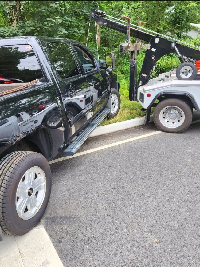 Black pickup truck being towed by a white tow truck on asphalt parking lot.