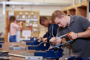 A man is cutting a piece of metal with a saw in a workshop.