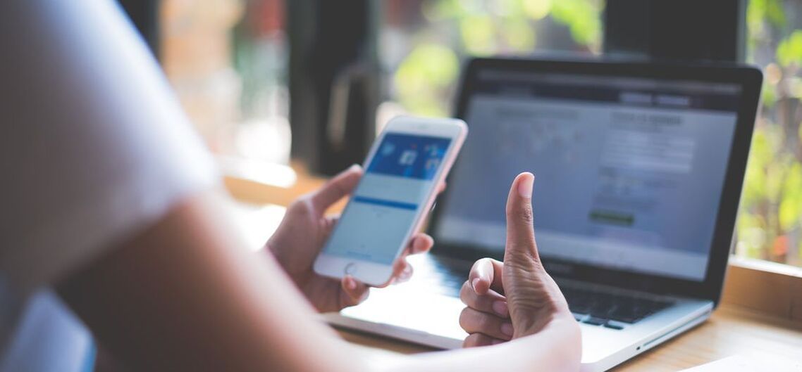 Photo of woman giving thumbs up to Facebook on her phone and laptop screens