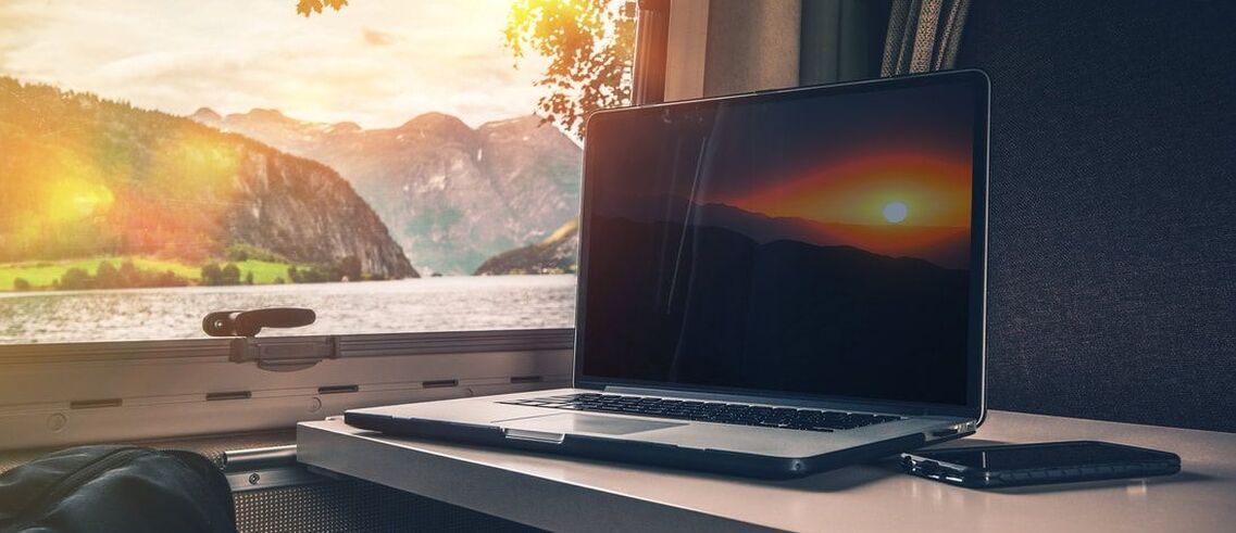 Laptop on train table with view of lake and mountain in window