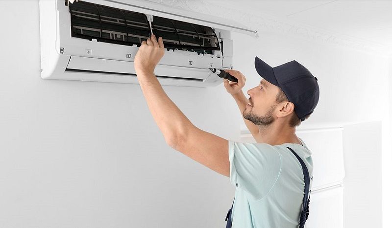 A man is fixing an air conditioner with a screwdriver.