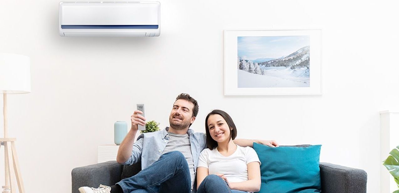 A man and a woman are sitting on a couch under an air conditioner.