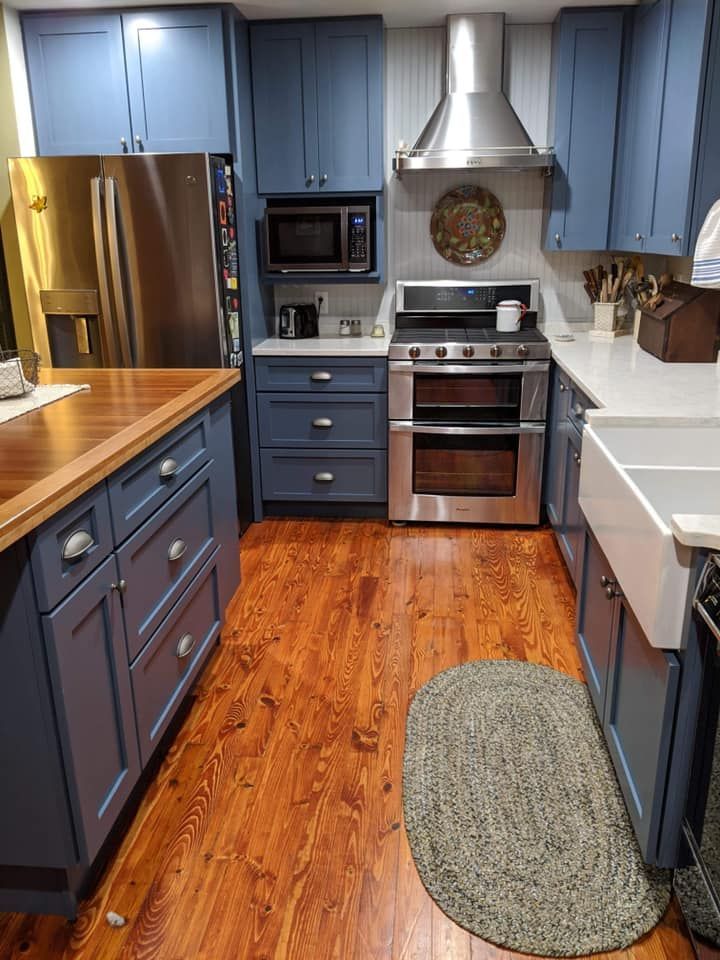A kitchen with blue cabinets, stainless steel appliances, a wood countertop on the island, and hardwood floors.
