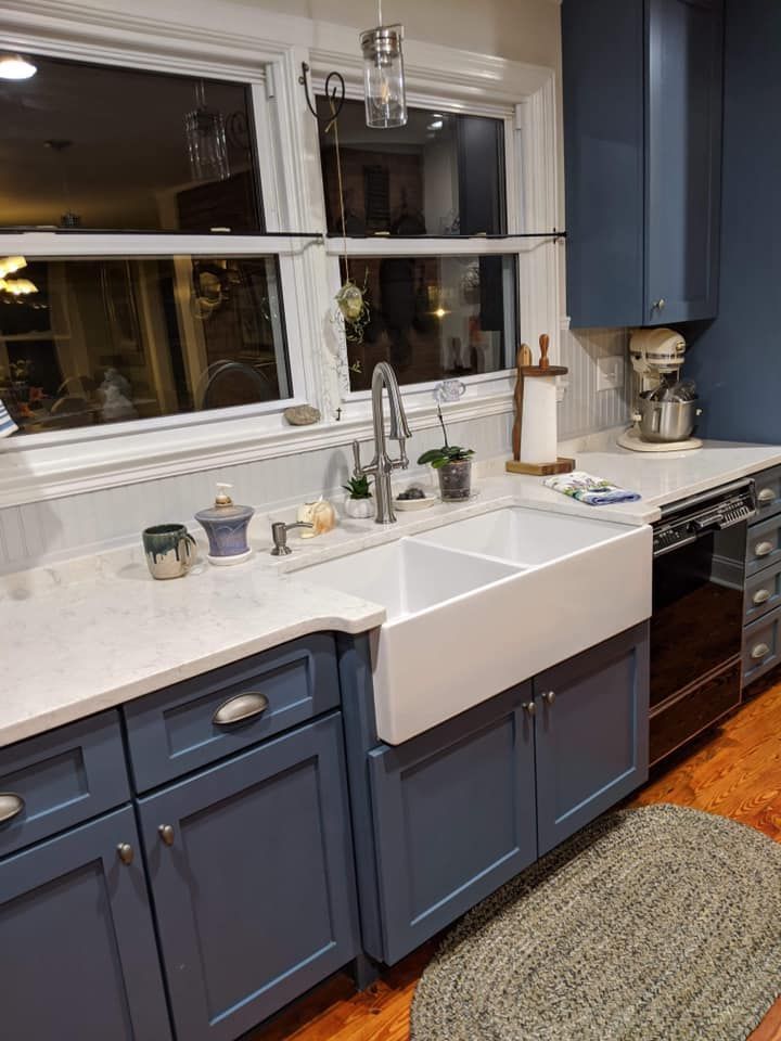 A kitchen featuring navy cabinets, a white farmhouse sink, light countertops, and a window above the sink.
