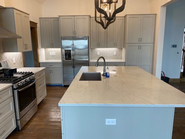 A kitchen with light gray cabinets, stainless steel appliances, a large central island, and a decorative light fixture.