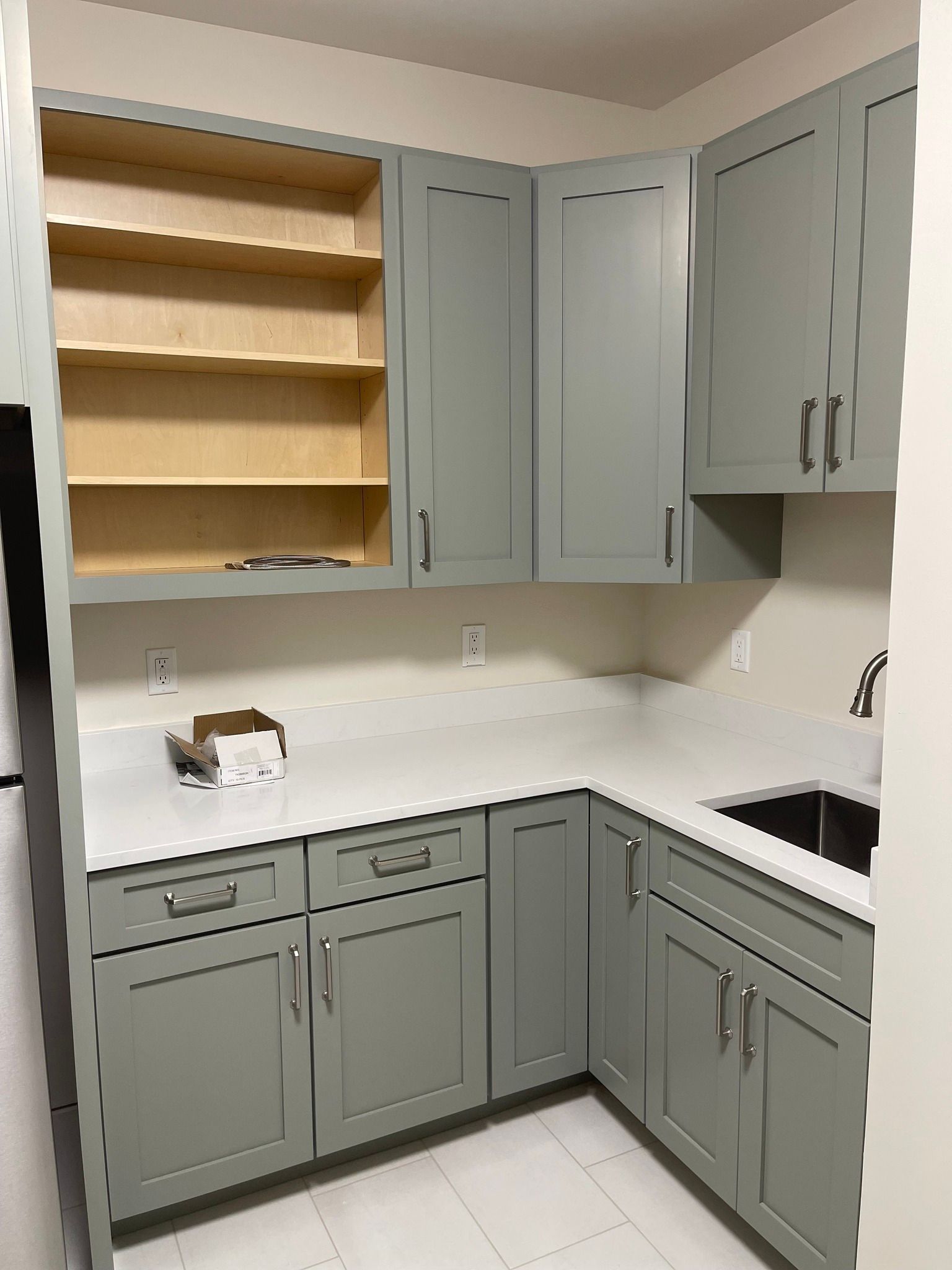L-shaped kitchen corner featuring sage green cabinets, white countertops, and open shelving.