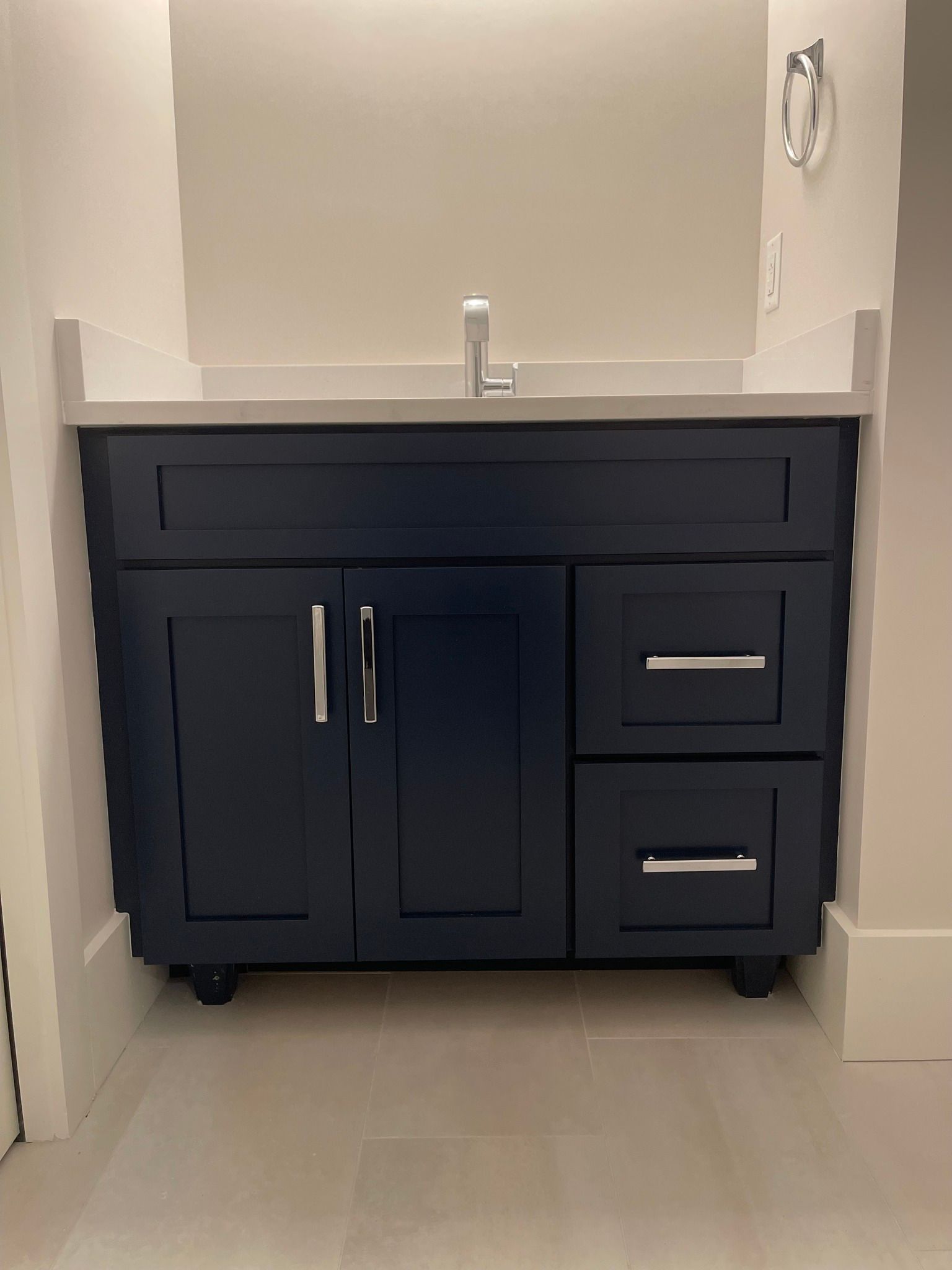 A navy blue bathroom vanity with a white countertop and silver hardware, set against light beige walls.